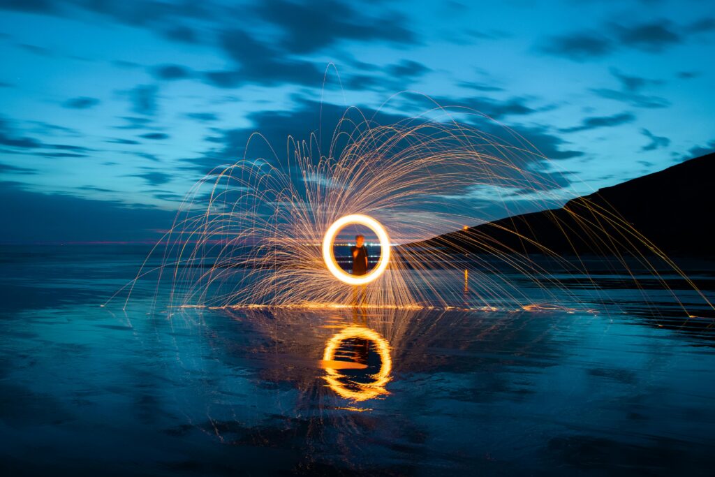 Enchanting steel wool photography with sparks illuminating a seaside landscape at night.